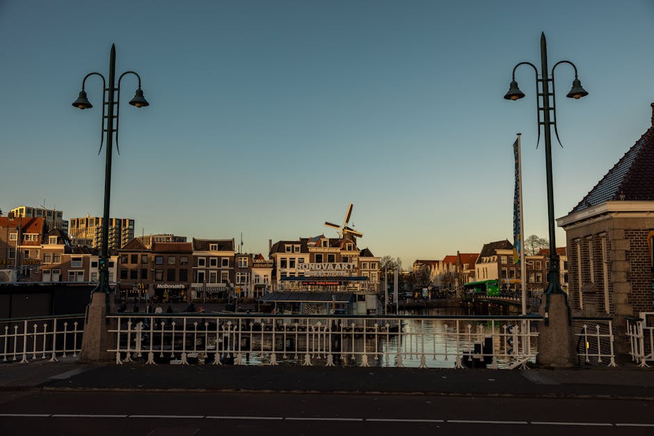 Picturesque Leiden cityscape with canal, bridge, and windmill at twilight. Historic Dutch architecture under a clear sky.
