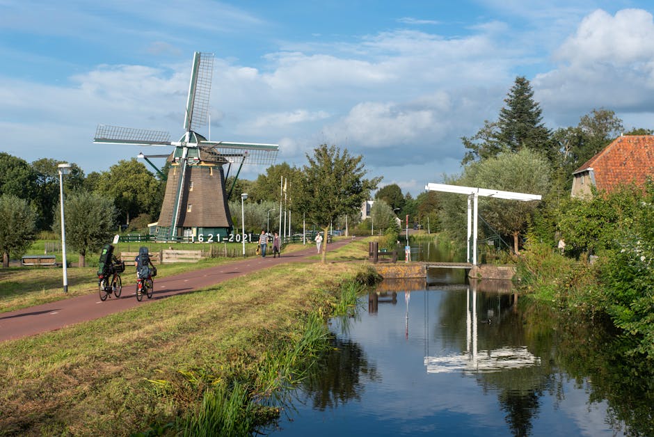 Cyclists enjoy a sunny day on a bicycle path near a historic windmill in Voorburg, Netherlands.