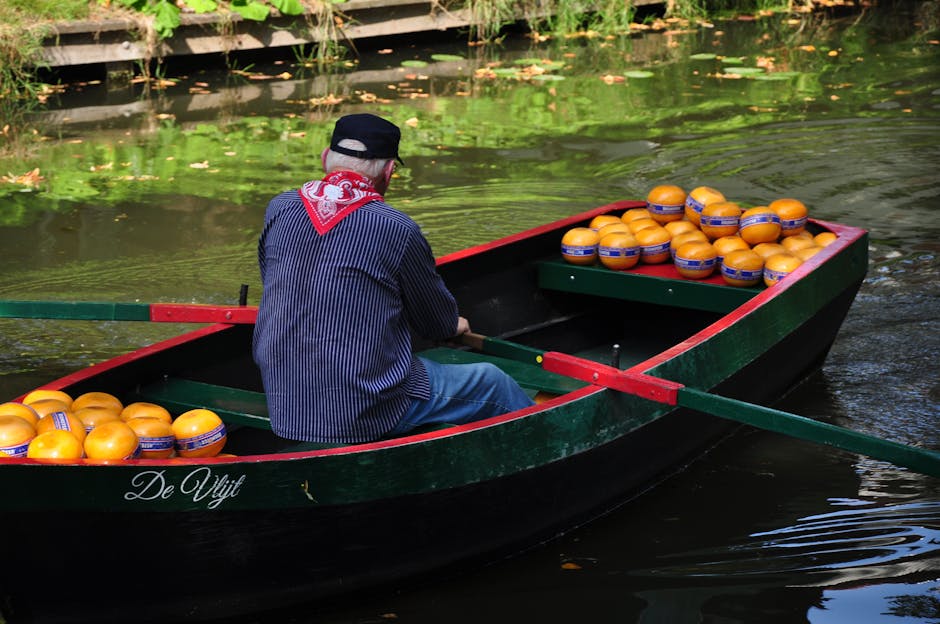 A Dutchman rowing a cheese-laden boat through an Amsterdam canal on a sunny day.