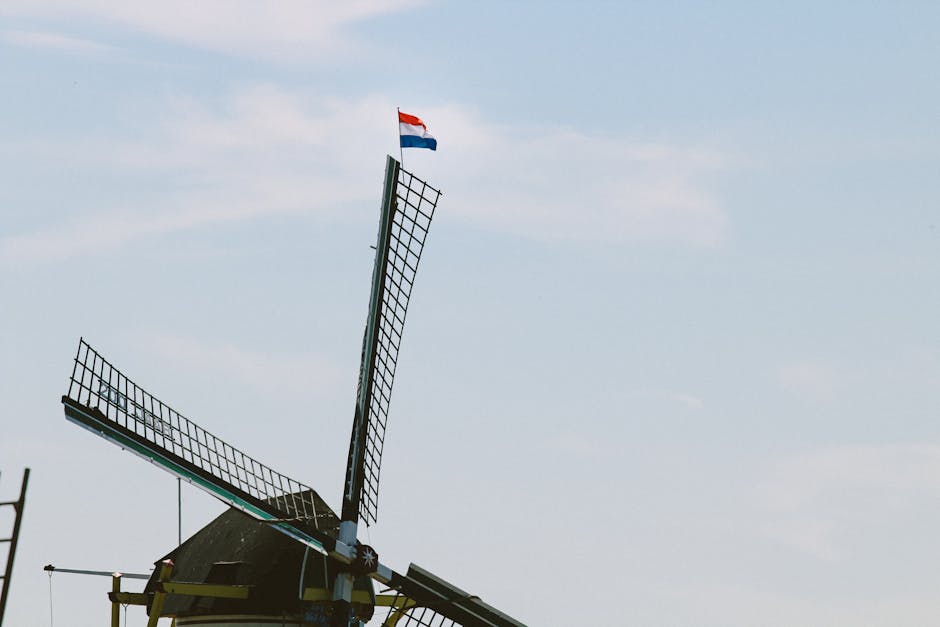 A classic Dutch windmill adorned with the Netherlands flag against a bright blue sky.