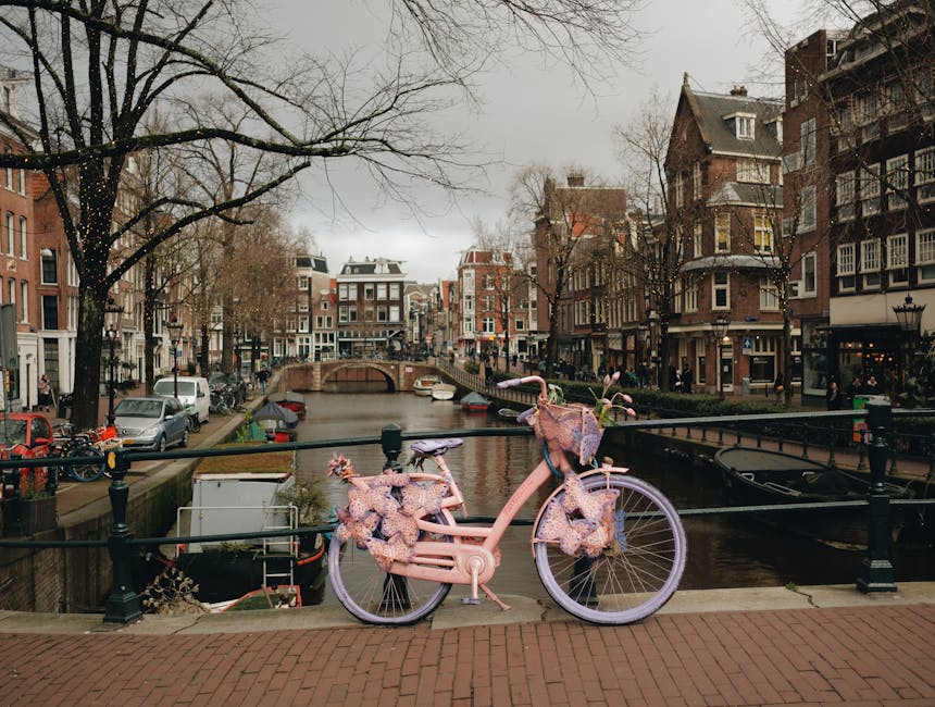 A picturesque Amsterdam cityscape featuring a canal, historic townhouses, and a decorative pink bicycle.